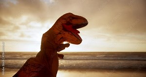Dinosaur costume, funny and boxing at beach with workout, and performance and fight air at sunset. Ocean, fitness and t rex costume with punch for energy, entertainment or cardio training in nature