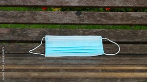 blue disposable protective mask, used for protection against cornavirus, thrown on a wooden bench in Rio de Janeiro.