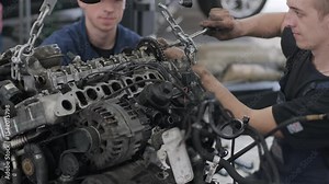 Mechanics removing engine using hoist in auto service workshop.