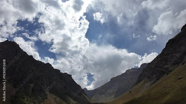 4K Mountain Landscape Front View from Below, Majestic Ranges on Both Sides of a Valley, Lush Grass on Peaks, Black Stones Below, Dynamic Motion Clouds, and Stunning Sky for Nature Tourism