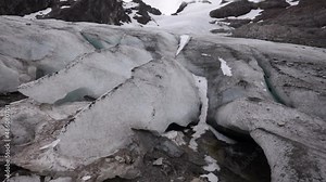 Alpine landscape. Glacial meltdown. View of the ice fields, rocks, mountain, peak, glacier cave and subterranean melting water rivers flowing downhill.