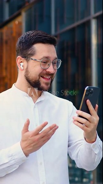 Attractive businessman wearing white shirt is on a video cal,l meeting conference influencer, entrepreneur business city while walking. He is holding his phone in one hand and use wireless headphones