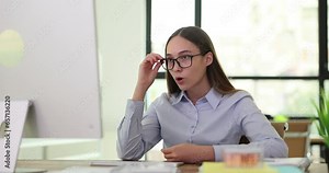 Office worker with confused and surprised expression looks at computer monitor. Employee removes glasses reading shocking news slow motion
