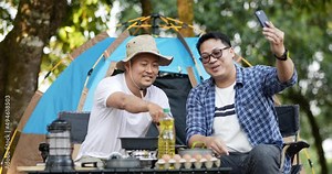 Portrait happy Asian man friends recording video live streaming online while cooking in camping. Cooking set front ground. Outdoor cooking, traveling, camping, lifestyle concept.