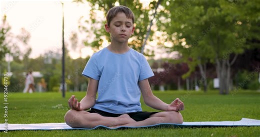 Active kid boy exercises on summer lawn. Sporty kid does yoga training in sunny park. Fit kid holds balance in lotus position. Outdoor fitness and physical health care activity for children.