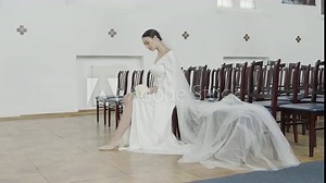 Brunette bride in fashion white wedding dress with makeup. Action. Wedding day of bride, woman sitting on a chair in front of empty rows.