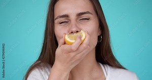 Young girl eats a lemon. Portrait of a beautiful woman. Girl grimaces while eating a sour lemon. Slow motion. Turquoise background.