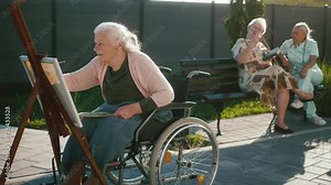 An old 90s grandmother in a wheelchair painting and admiring her work in the yard of a geriatric center