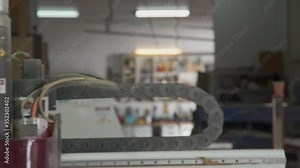 Close up view of CNC router arm operating. Large hose used to vacuum dust and debris from cutting surface while robotic arm moves router along cutting path. Danger sign on power tool.