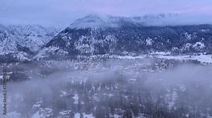 Fog is creeping above Bavarian village. Winter wonderland in Leavenworth with Cascade Mountains on background. Aerial winter season Leavenworth Washington. Drone flying through cloud on winter evening