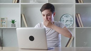 Scared boy shocked by terrible scene while reading horror news on computer. Afraid schoolboy kid look at monitor screen, cover mouth with his hand while using laptop sitting at desk at home. Stock Video