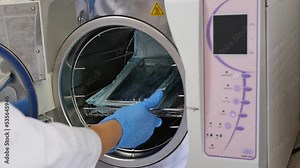 the hands of a medical orderly remove a medical operating instrument that has been cleaned and sterilized by ultrasound from the autoclave. medical instrument disinfection in ultrasonic autoclave