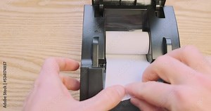 Replacing the thermal paper roll in a receipt printer. First person view, hands inserting the roll into the printer.