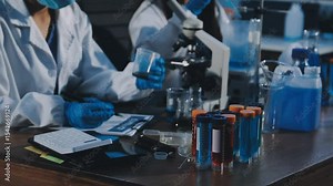 Technician holding blood tube test in the research laboratory / doctor hand taking a blood sample tube from a rack with machines of analysis in the lab background