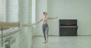 Graceful classic ballet dancer practicing tombee exercise at barre during rehearsal in ballet studio. Ballerina performing different choreographic exercises and dance moves in dance studio.