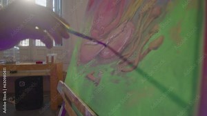 Talented male painter using oil paint and brush, drawing buddha on canvas and easel set, working in sunlit art studio during the day. Handheld camera shot