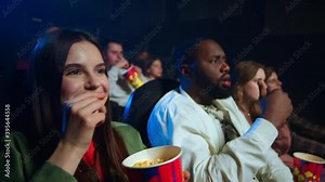 Scared friends looking film in dark hall. Shocked people jumping in cinema.