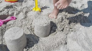 Child breaking sandcastles. The child's feet are crushing the sand structure.