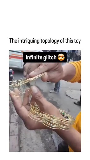 wowmemes_s on Instagram: "The post showcases a video of an Indian street vendor spinning a mesmerizing toy made from interlocked golden wire rings with colored beads, producing an optical illusion dubbed "infinite glitch" that captivates viewers through rapid rotation. This toy is a disentanglement puzzle rooted in topology, akin to the classic Chinese Rings, where rings link in sequences requiring precise moves to separate, demonstrating mathematical concepts of knot theory and invariant linkin