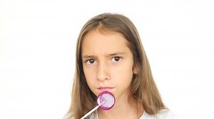 A little girl licks a lollipop stares into the camera and makes funny faces. 4k, slow motion, copy space