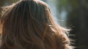 Close-up rear view of beautiful blonde hair in nature. Stock footage. Beautiful blonde woman's hair with sunny summer rays. Blonde woman with wavy hair in forest on sunny summer day