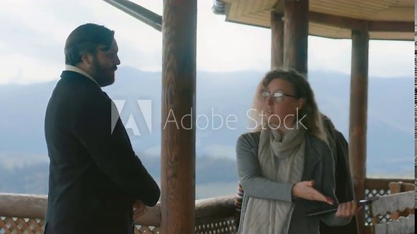 Professional real estate agent with tablet computer shows potential new home property to family with kids. Female realtor discusses renting or buying house with mountains view with man. Slow motion.