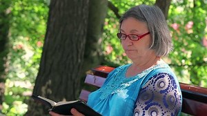 Senior woman reading bible on the bench in the park.