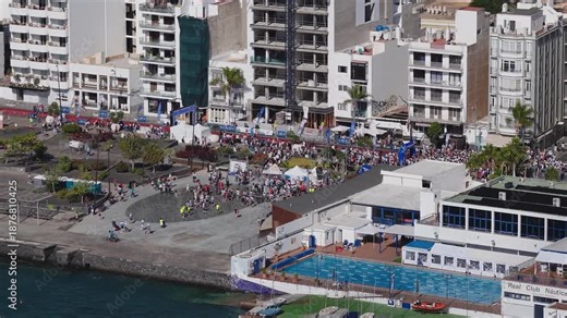 Aerial wide view shows Arrecife promenade in Lanzarote with the 2025 Lanzarote International Marathon, red carpet, white tents, toilets, garden figures, solar panel pergolas.