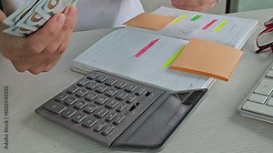 Closeup of woman hand using calculator and stacks of dollar bills