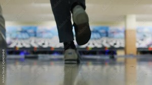 Close-up bottom view of skullful excited young man throwing bowling ball in the alley. Friends playing bowling together in bowling club.