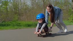 Junge Mutter reitet ihren Sohn auf einem Skateboard, während er...