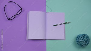 Video of a book's page turning stop motion on colored background with different office stuff. Blank template for words inside an open purple notebook. Writing and creative concept