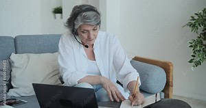 Smart and motivated retired old woman using laptop and earphones to learning new skills over the Internet online. Webinars, tutorials and video conferences are a perfect way for seniors to study.
