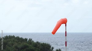 Windsock blow in wind to show speed and direction of wind gusts. Windsock with cloudy sky in the background. Conical tube in fabric used as a basic guide for the direction and speed of the wind.