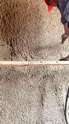 Applying rough cement plaster texture to wall surface using specialized spray machine