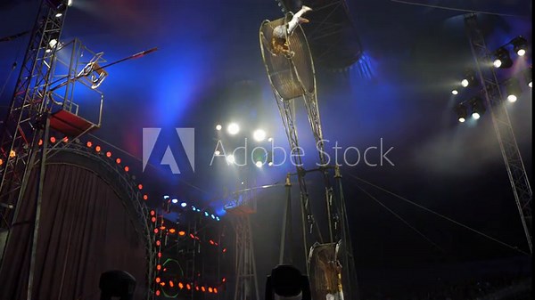Two brave male acrobats in a rotating wheel of death perform under the dome of the circus in the light of bright concert lights and smoke. A dangerous acrobatic act on a rotating wheel. A circus act.