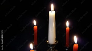 Christmas candles burning with one standing out from the crowd in center on holy evening and new year’s day on ancient candleholder candlestick isolated on black background while flames waving and mov