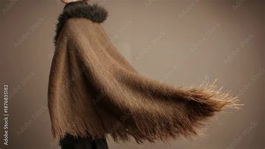 Starting torso rotation, model sweeping arm under fringed cape at studio, showing cape billowing