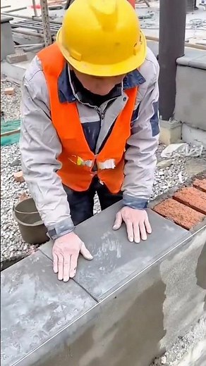 laying a line of grey rectangular stone tiles onto a brick wall at a work site