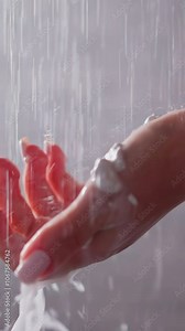Woman holds foamy palm under shower sprays closeup. Lady washes body with skin moisturizing mouse for spa procedures in bathroom. Skincare cosmetic
