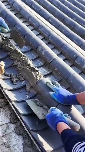 Workers cement roof carefully showing precise tile method