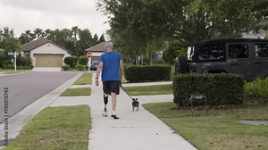 Older adult male from the back walking his dog while using his prosthetic leg