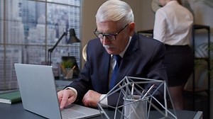 Coworking. Focused business man entrepreneur typing on laptop doing research. Senior professional using computer sitting at office desk. Busy worker freelancer working on modern tech notebook device