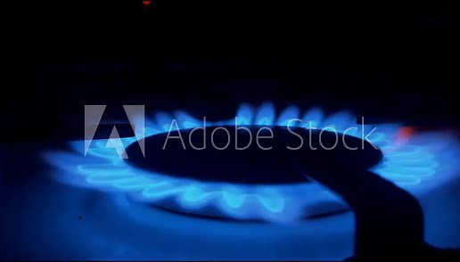 A blue fire lights up in the burner of the gas stove in complete darkness. The stove uses combustible or natural gas from the city gas network or liquefied gas as fuel.