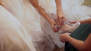 A bride putting on her shoes before leaving for the wedding with the help of her wedding assistant
