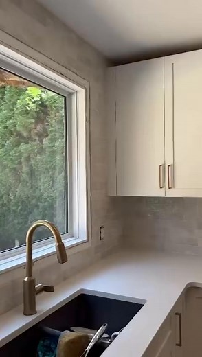 This kitchen remodel features a modern and sophisticated design with a neutral gray and white color scheme. Key elements include light gray, glossy subway tile for the backsplash, sleek white countertops, and a striking gold pull-down faucet paired with a dark undermount sink. This design successfully balances classic elements with modern trends, creating an elegant and functional cooking space. #VancouverRenovation #CustomTiling#LuxuryBathroom #BathroomDesign #TileWork #ModernBathroom #Bathroom