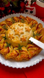 Delicious sheets of puff pastry filled with pesto sauce and camembert, makes this Christmas Wreath the perfect recipe and addition to your holiday menu. It is so much easier to make than it looks and is guaranteed to get lots of aahs and oohs from the guests. Ingredients: -2 sheets puff pastry -1 whole baking camembert or brie -3 tablespoons pesto -3 tablespoons grated mozzarella or cheddar -1 beaten egg Instructions: 1. Preheat the oven to 220 C. 2. Cut both puff pastry sheets into circles. Pla