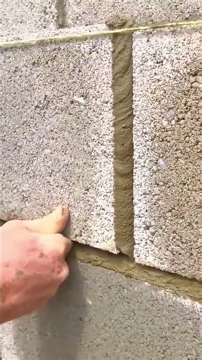 handheld metal spade to apply a thin layer of wet grey mortar onto a long row of grey bricks