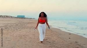 Beautiful African american woman in bikini on tropical beach. Portrait of dark skinned woman smiling at sea. Brunette tanned girl in swimwear enjoying and walking on beach.