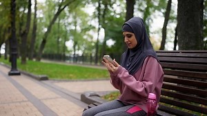 Young Arab woman texting on smartphone during morning training break in park